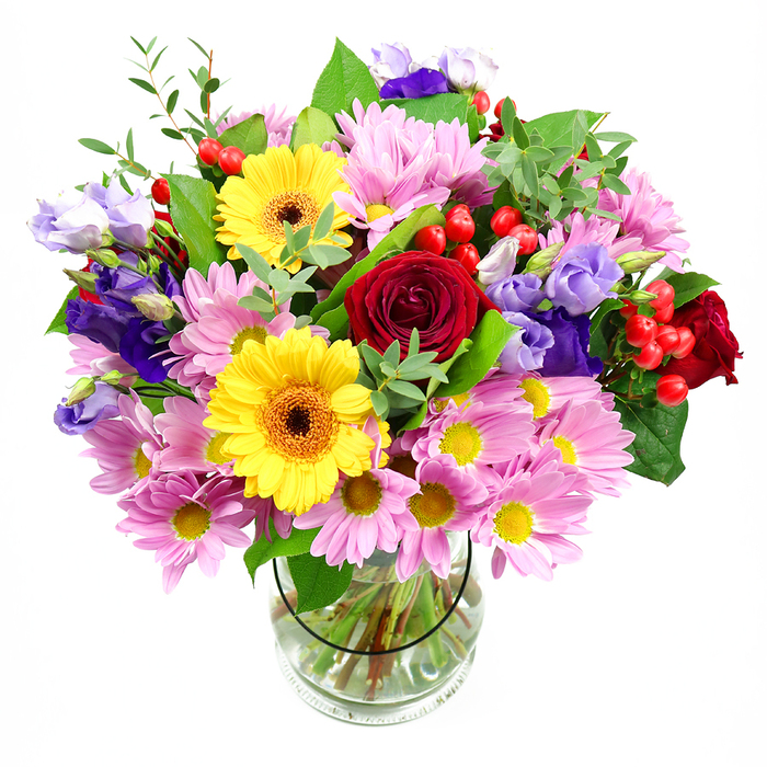 A richly textured bouquet of mixed flowers stands tall in a clear glass vase, photographed against a simple white background that allows the intricate colours and forms to take centre stage, much like a statement piece in a Brentwood home. At the centre sit deep red roses, their velvet-soft petals curling inward in perfect spirals, creating a sense of depth and heartfelt emotion. To one side and the other, two bright yellow gerbera daisies with dark brown-orange centres add a sunlit accent, their flat, daisy-style blooms radiating a lively, upbeat charm. Encircling these main flowers are abundant clusters of soft pink daisies or chrysanthemums, each head filled with many slender petals and a small yellow centre, building a cloud of pastel tones that softens the stronger colours. Woven intuitively through this base are purple and lavender lisianthus, their bell-shaped flowers and gently ruffled edges adding cooler hues and an elegant, slightly whimsical feel, akin to a walk through the green spaces near King George's Playing Fields in Brentwood. Here and there, clusters of glossy red hypericum berries peek out, offering a distinctive, rounded texture that catches the eye and complements the reds and pinks. The design is bound together by a variety of foliage in different shapes and greens - some broad and deep-toned, others lighter and more delicate - which frames the blooms and gives the arrangement a fresh, natural structure. The glass vase is crystal clear, revealing the tidy stems and fresh water beneath, a quiet testament to professional floristry skills. Overall, the bouquet radiates joy and warmth, suitable for celebrating milestones, saying thank you, or simply adding a splash of colour to everyday life in Brentwood.